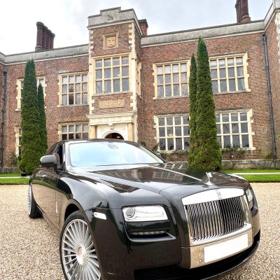 Black Rolls-Royce Ghost parked outside a Tudor manor house
